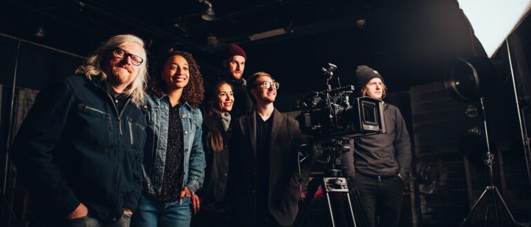 Filmproduzent Jobs: Gruppe von Filmschaffenden steht hinter einer Kamera am Set, darunter Produzenten, Schauspieler und Crew-Mitglieder in der Filmbranche.